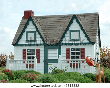 Gingerbread House in the Garden - A small garden shed that looks like a play house sits in a garden of mums in the springtime.