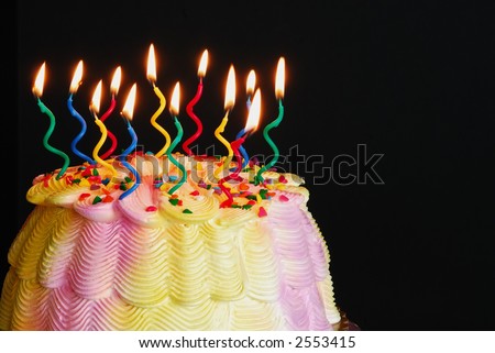 Lighted Birthday Cake - Burning candles on a pink and yellow iced birthday cake in front of a black background.