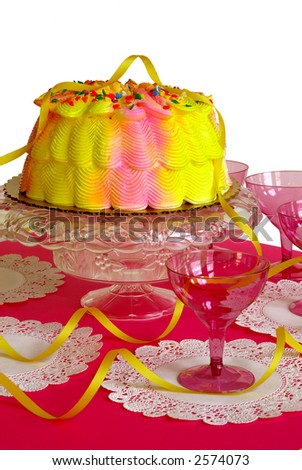 Birthday Cake - A pink and yellow iced birthday cake on a table decorated with yellow ribbons, pink stemware and white lace doilies