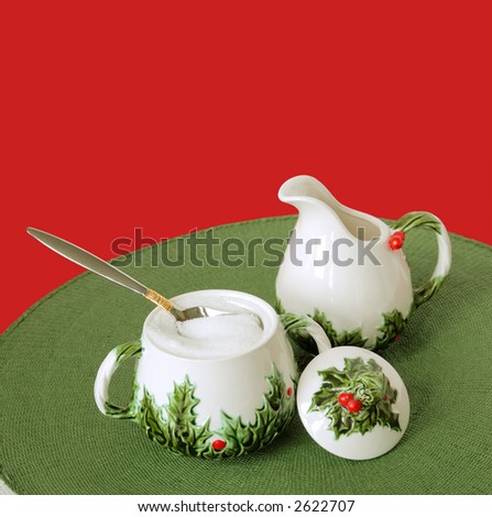 Vintage Christmas Holiday Creamer and Sugar Bowl sitting on a green woven placemat against a red background.