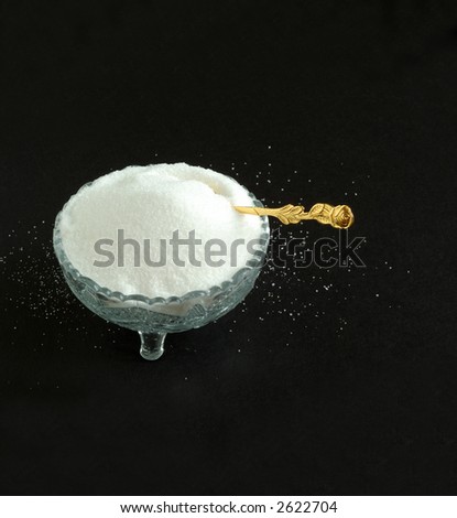 Pure White Granulated Sugar on a Black Background - Pure snowy white sugar in a vintage crystal bowl with a gold spoon sitting on a sugar covered black textured background.