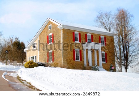 Colonial Farmhouse in Winter - A colonial style stone house sitting on a snow covered hill on a sunny winter day.