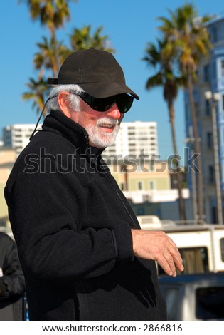 Smiling Man Portrait -  a smiling man in black sunglasses, a jacket and ball cap, standing outside on a beautiful sunny day.