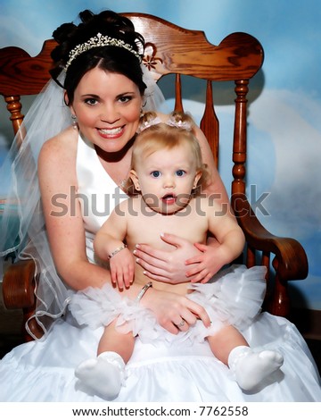 Preparing For The Wedding Ceremony - Bride holding a baby while seated in a chair.  The baby is surprised and the bride is smiling.