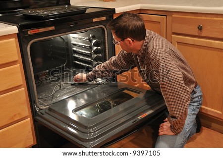 A man kneeling on the kitchen floor and cleaning the inside of an oven.