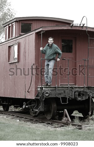 Man On The Train Caboose - Man standing on the back of an old train car caboose, leaning on the rail.