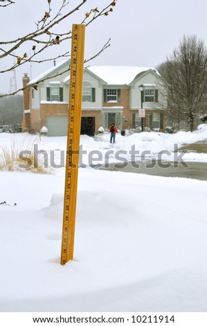 15 inches of Snow measured by a yellow yard stick in a snow drift with a man shoveling out his driveway in the background.