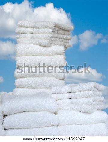 Fresh As Spring - A stack of folded white towels and wash cloths outside against a bright blue sky with white puffy clouds.