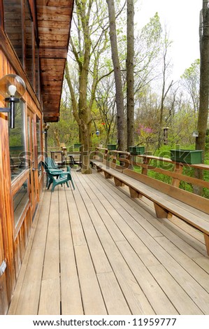 A large deck on the outside of the back of a residential house in a wooded setting.