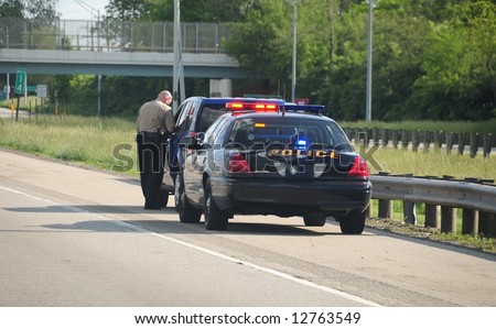 Traffic Ticket Police Vehicle - A police cruiser with the lights flashing has stopped a speeding car along the interstate highway and is issuing a ticket.