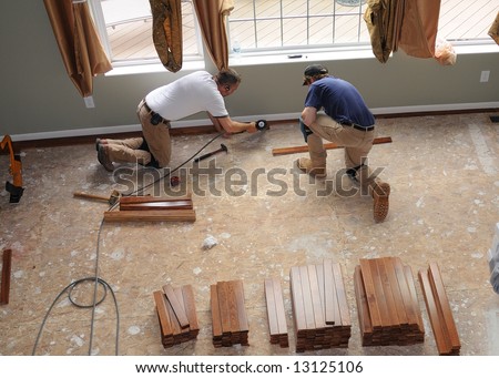Hardwood Floor Installation - Construction workers install a hardwood floor over oriented strand board in a residence.