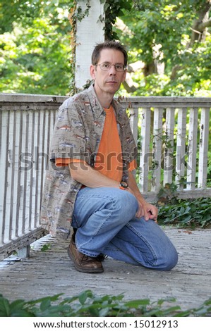 Man wearing glasses, kneeling on an old deck.