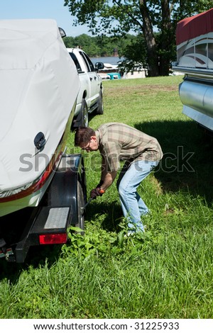 A man is tightening the lug nuts on a boat trailer wheel for safety in traveling to the lake.