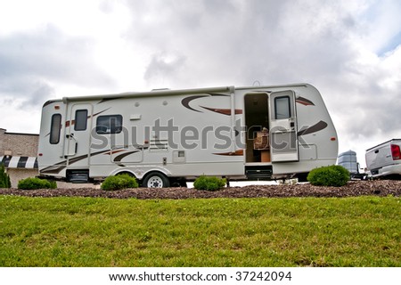 A travel trailer sits on a hill with the door open and a dog seated on the bed inside.