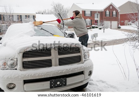 A man using a broom to sweep snow off the windshield of his truck after a winter storm.