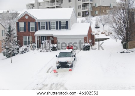 A pickup truck equipped with a plow and a salt thrower is removing snow from a sloped driveway in winter.