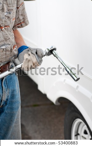 A man holding a torque wrench socket and extension in a gloved hand, ready to tighten the lug nuts on a truck.