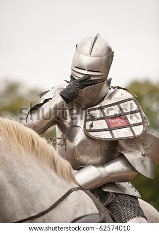 Knight in Shining Armor - medieval renaissance knight in full armor adjusting his face mask while sitting on his horse.