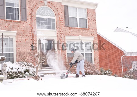 A man uses a snow blower to clear the freshly fallen snow off the sidewalk in front of his house in winter.