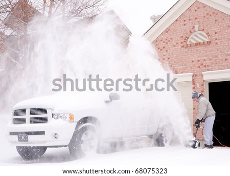 A man uses a snow blower to clear the freshly fallen snow off the driveway in front of his house in winter.