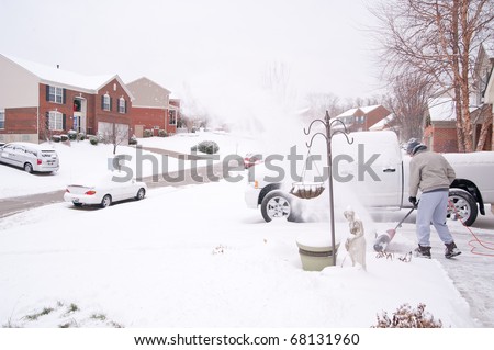 A man uses a snow blower to clear the freshly fallen snow off the sidewalk and driveway in front of his house in winter.