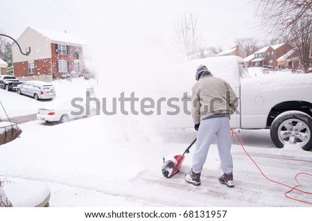 A man uses a snow blower to clear the freshly fallen snow off the sidewalk and driveway in front of his house in winter.