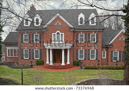 A brick three-story home in a secluded wooded location on a dark and dreary winter day.