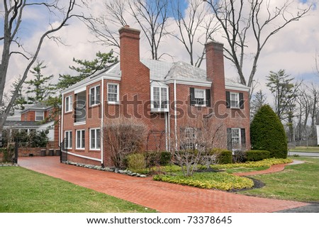 Brick Suburban 2-Story Home on a rainy spring day.  The terra cotta shades of the cobblestone driveway coordinate with the brick on the exterior of the house.