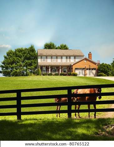 Two story home with a mare and a pony standing along the fence in front of the house in the front yard in Kentucky, USA.