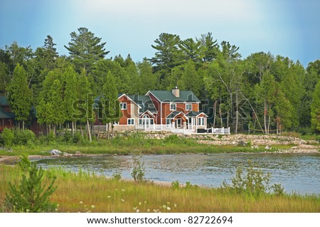 A red cedar shake, two-story vacation home nestled in the pine trees on lakefront property in summer.