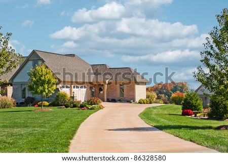 Modern brick, stone and shakes two story house in USA with a concrete driveway leading to a side entry garage in autumn.