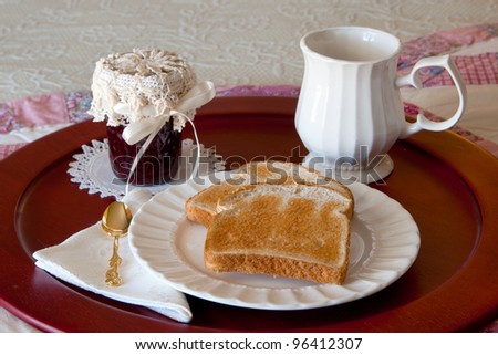 Breakfast tray holding two pieces of dry toast on a white plate with a jar of raspberry jam, a jelly spoon on a linen napkin and a coffee cup next to it.