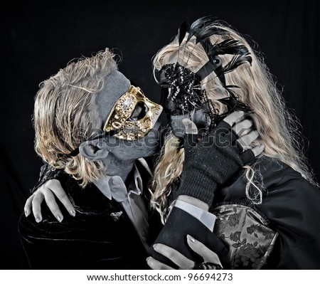 Vampire Kiss - A young couple dressed as goth vampires wearing masks and dark clothing, embrace in a kiss.