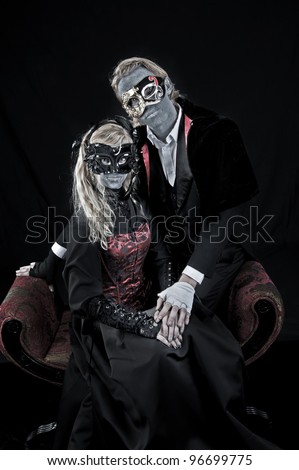 Young gothic vampire couple posing for a portrait wearing vintage costumes, makeup and masks.