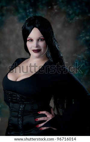Sexy Goth Girl - beautiful young woman with long black hair is posing in a low-cut dress with goth style makeup, hair and clothing.