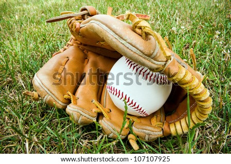 a baseball and an old baseball glove lying on the a baseball field.