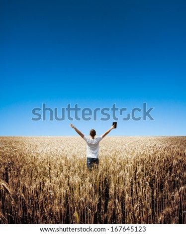 man holding up Bible in a wheat field