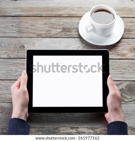 female hands holding digital tablet computer with isolated screen over old grey wooden background table with a cup of black coffee on the background