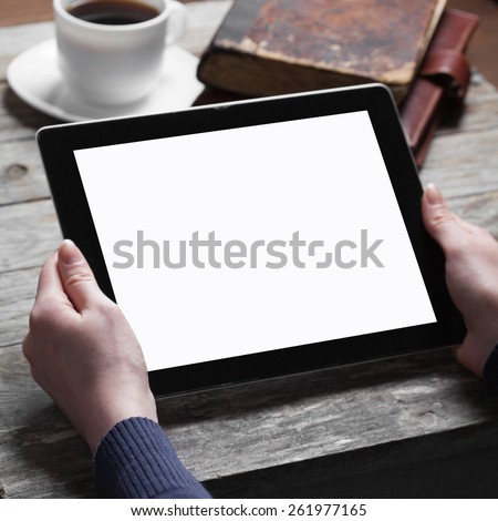female hands holding digital tablet computer with isolated screen over old grey wooden background table with a cup of black coffee and an old book on the background