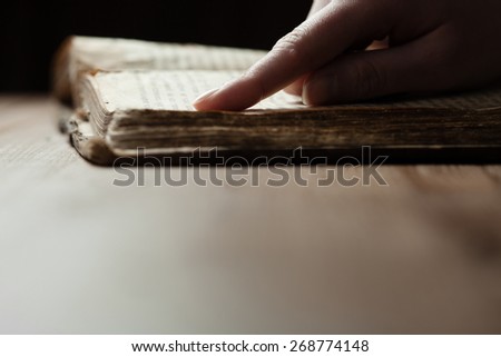 woman finger presses on old bible book in a darkness over wooden table and reading a bible