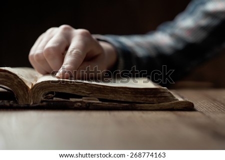woman finger presses on old bible book over wooden table and reading