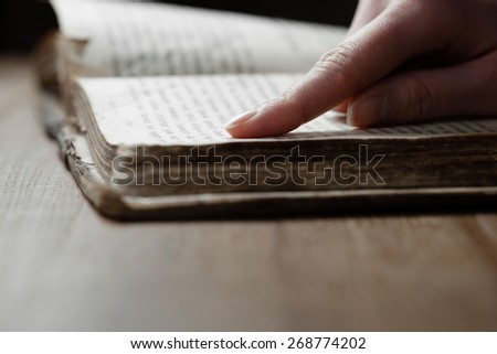 woman finger presses on old bible book in a dark room over wooden table and reading a bible