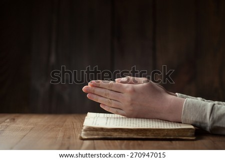 Hands folded in prayer over open russian Holy Bible