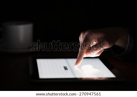 oman hand presses on screen digital tablet in the darkness