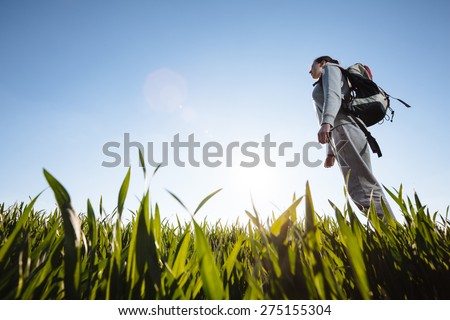 woman hiker with backpack walking through the grass meadow