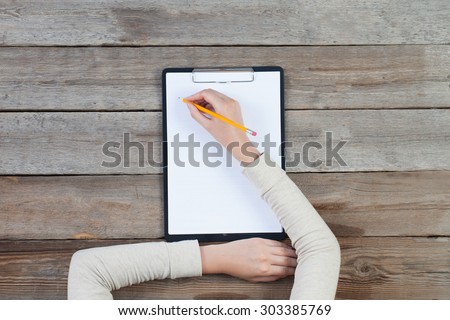 woman\'s hand writing on paper over wooden table