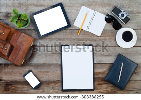 Black tablet computer ipad style and smart phone with isolated screens on old wooden desk with diffrent objects around