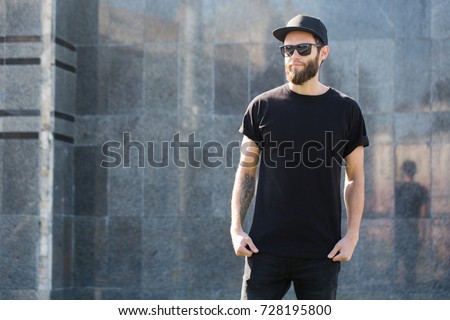 Hipster handsome male model with beard  wearing black blank  t-shirt with space for your logo or design in casual urban style