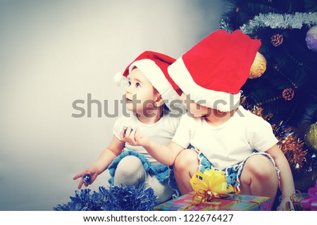 Two cute little girl sitting with gifts under the Christmas tree