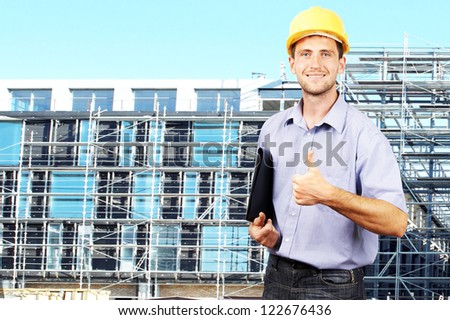 Young smiling businessman in his helmet against the backdrop of the building under construction